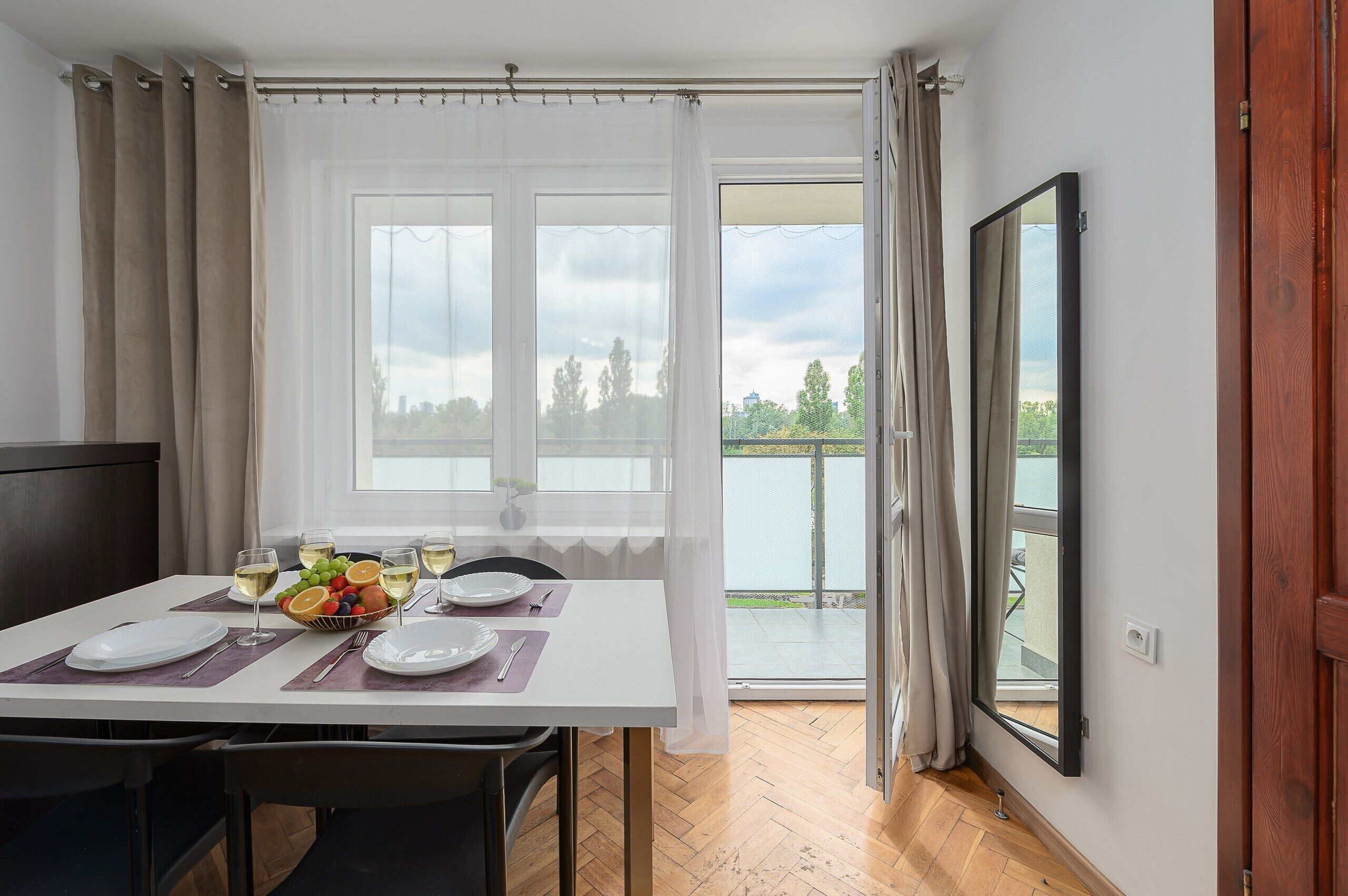 A dining area with a table set for four, a window with a view of a balcony, and a door leading outside.
