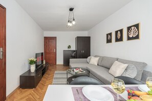Ein modernes Wohnzimmer mit grauem Sofa, einem Holzschrank, einem Fernseher und einem Essbereich mit einem Glastisch.