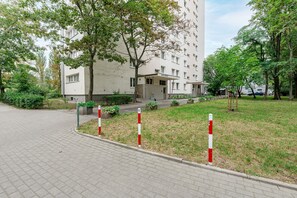 Ein Gebäude mit flacher Fassade, zahlreichen Fenstern und einem Schild, das es als Hotel kennzeichnet. Vor dem Gebäude befindet sich ein gepflasterter Bereich mit Gras und einigen Bäumen.