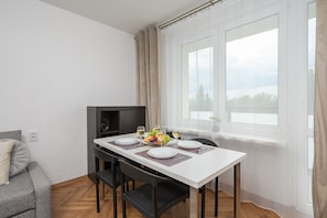 Uma área de refeições com uma mesa posta para dois, um sofá e uma janela com cortinas.