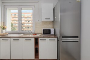 Eine moderne Küche mit weißen Schränken, einem Edelstahl-Kühlschrank, einer Mikrowelle und einem Fenster mit Blick auf ein Gebäude.