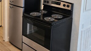 Eine Küche mit einem Edelstahl-Kühlschrank, einer Mikrowelle und einem schwarzen Herd mit vier Kochfeldern.