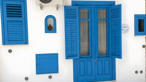 Eine Gebäudefassade mit blauen Fensterläden, einer zentralen Tür mit Glasscheiben und einem kleinen, rundbogigen Fenster mit Kreuzverstosung.