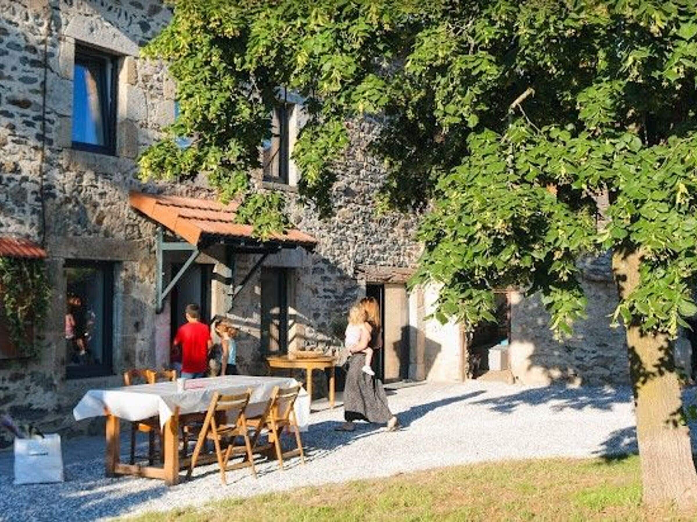 A stone building with a covered outdoor seating area, a gravel path, and a tree.