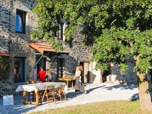 Ein Gebäude aus Stein mit überdachter Außenbestuhlung, einem Kiesweg und einem Baum.