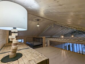 A loft bedroom with a sloped ceiling, a wooden floor, a bed with a metal frame, a hanging light fixture, and a view through a wire mesh. - Country house - 15 guests - Loire Valley (Retournac)