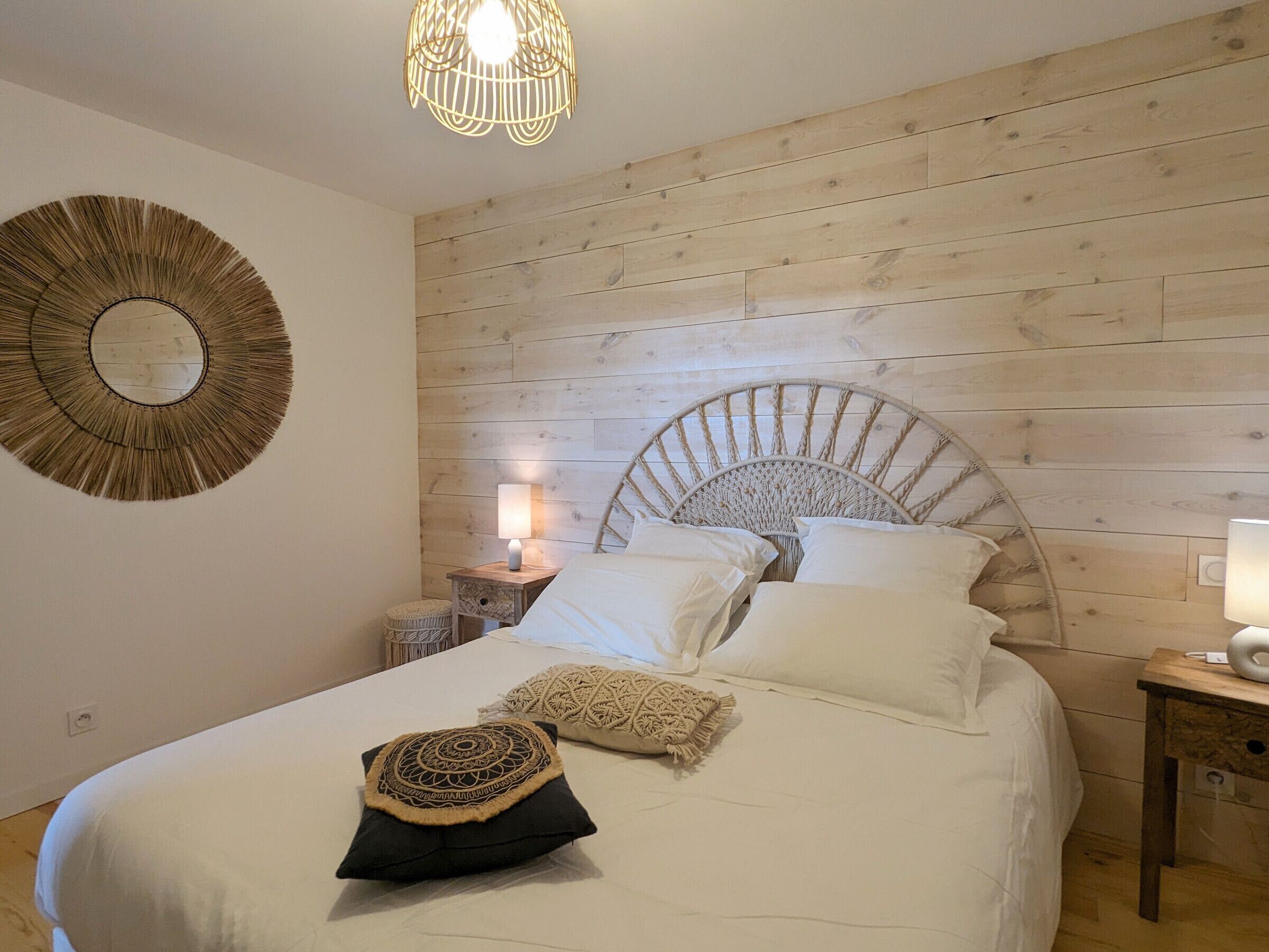 Un dormitorio con cabecera de madera, un espejo redondo, una lámpara de noche y ropa de cama blanca.
