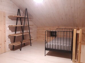 Ein kleiner Raum mit Holzboden, einem Etagenbett, einer Leiter und einem Regal.