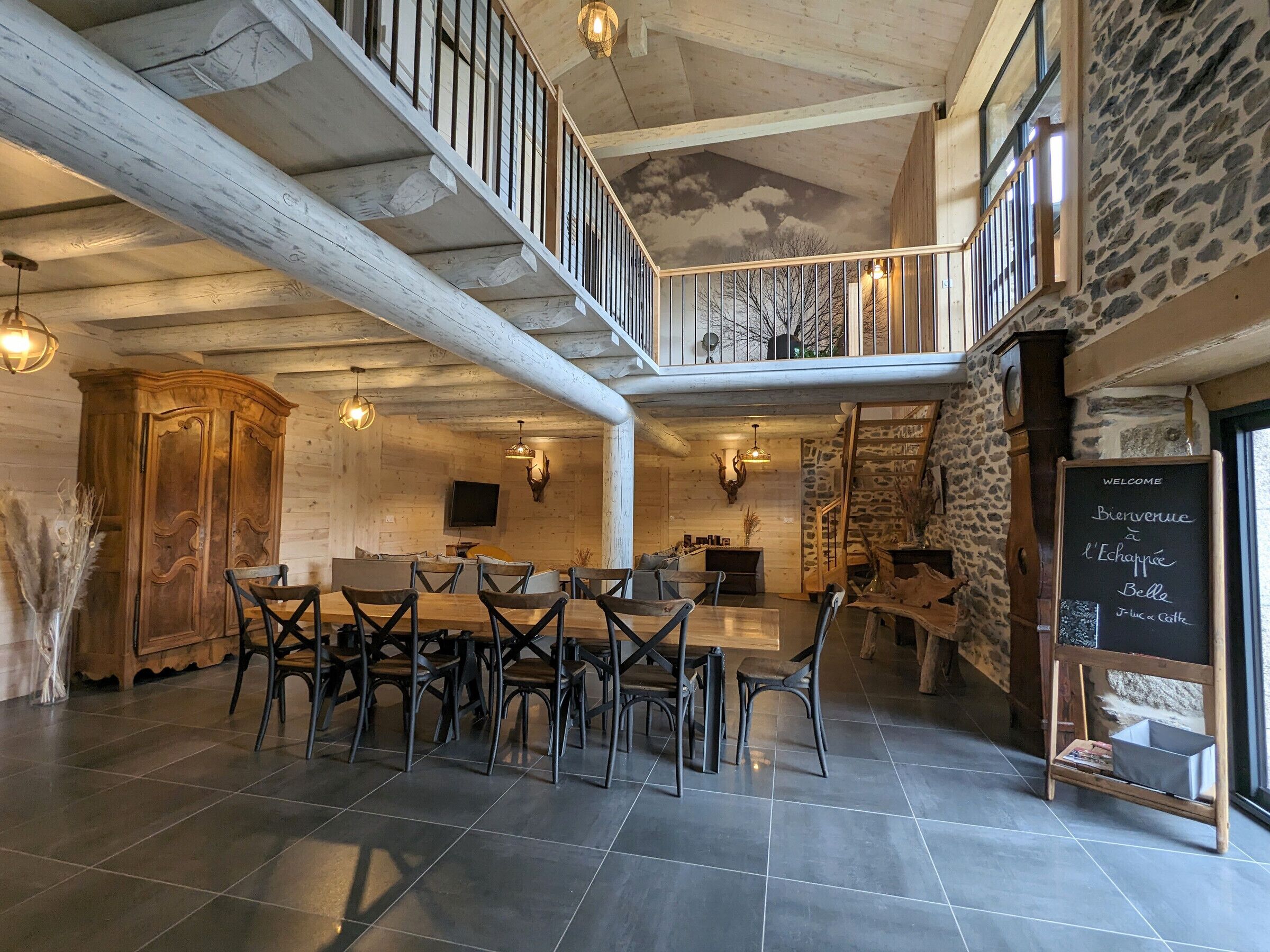 Une salle à manger spacieuse avec un plafond haut et des poutres apparentes, une table en bois avec des chaises et un escalier menant à un niveau supérieur.