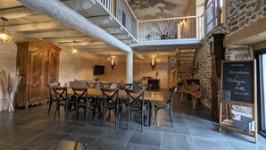 A spacious dining area with a high ceiling and exposed beams, a wooden table with chairs, and a staircase leading to an upper level. - Country house - 15 guests - Loire Valley (Retournac)