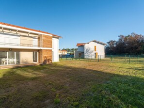 Ein modernes, zweistöckiges Haus mit Balkon, umzäuntem Garten und blauem Himmel.