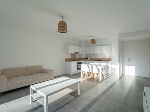 Ein zeitgemäßer Wohnraum mit Sofa, Esstisch mit Stühlen, Küchenzeile und einer Pendelleuchte.