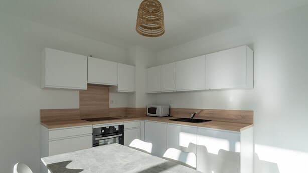 A modern kitchen with white cabinetry, a wooden countertop, a built-in microwave, and a dining table with chairs. - Modern apartment with parking - 4 guests (Mimizan)