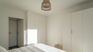 A bedroom with a large bed, a wardrobe, and a hanging light fixture. - Modern apartment with parking - 4 guests (Mimizan)