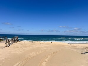 Ein sandiger Strand mit einer hölzernen Promenade, die zum Meer führt.