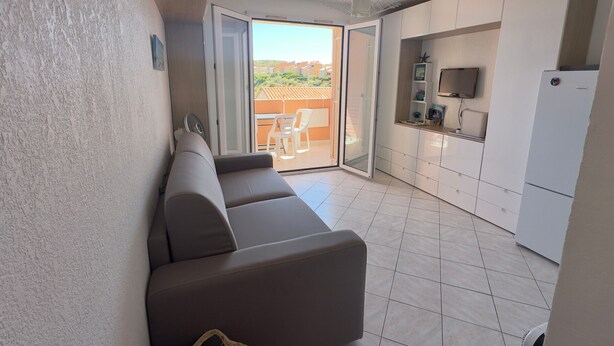 Eine moderne Wohnung mit einer Couch, einer Küchenzeile und einer Schiebetür zu einem Balkon.
