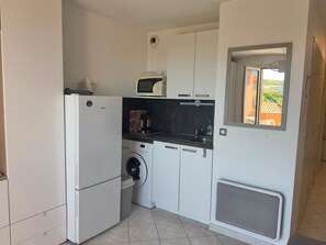 A compact kitchen with a washing machine, a microwave, and a small sink. - Charming sea view T2 with private parking (Collioure)