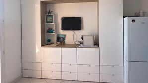 Eine kleine Küche mit integriertem Fernseher, einem weißen Kühlschrank und einem Regal mit Dekoration.