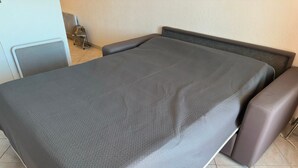 Ein Bett mit grauer Bettdecke und zwei braunen Sesseln.