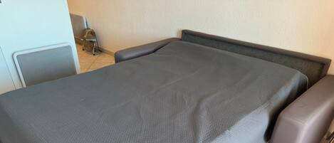 Una cama con un edredón gris y dos sillones marrones.