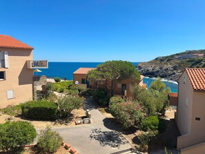A coastal residential area with terraced houses, a clear view of the sea, and a paved courtyard. - Charming sea view T2 with private parking (Collioure)