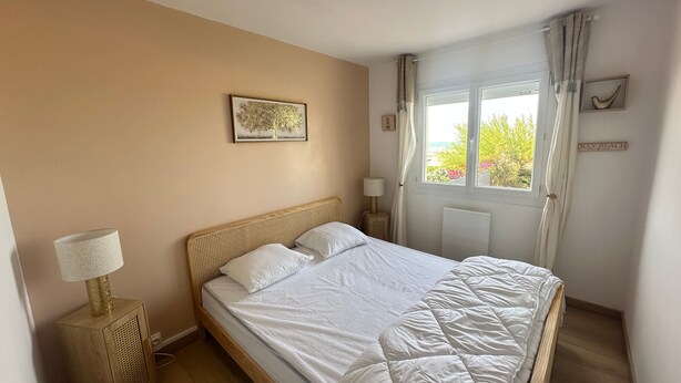 Une chambre à coucher avec un lit, des lampes de chevet, une fenêtre avec des rideaux, un tableau accroché au mur et une affiche sur le mur.