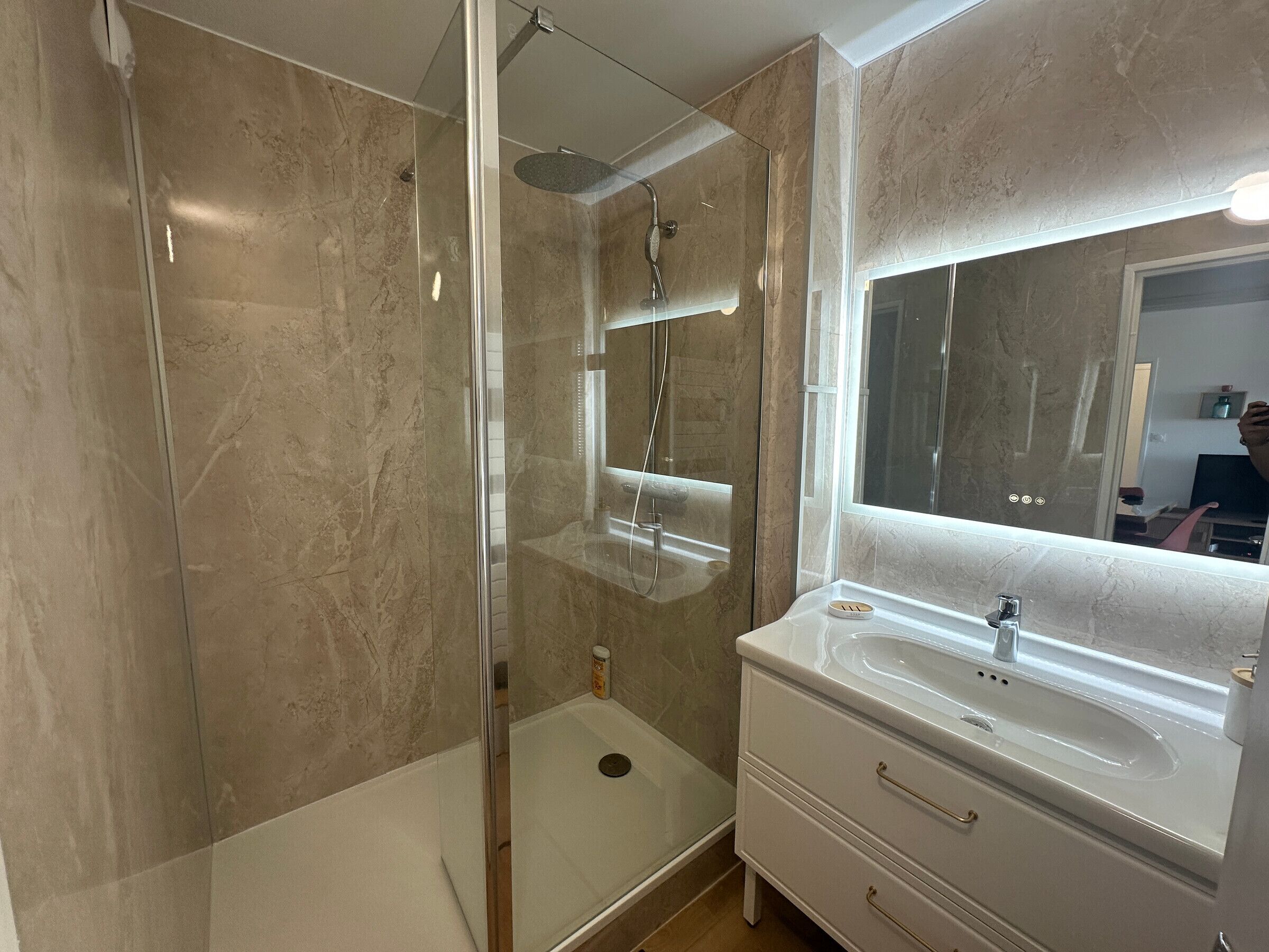 A bathroom with a glass-enclosed shower, a sink with a mirror, and a vanity with drawers.