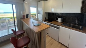 Une cuisine moderne avec un plan de travail en bois, des armoires blanches et une vue sur la plage.