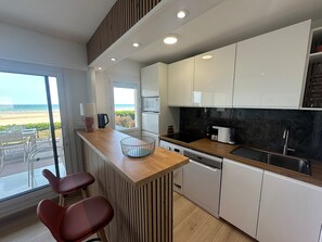 A modern kitchen with a wooden countertop, white cabinets, and a view of the beach. - Apartment, sea view, pets welcome - 4 guests (Cabourg)