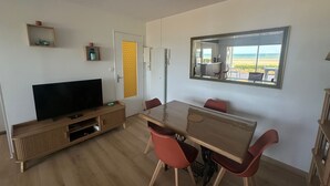 Un salon moderne avec un téléviseur à écran plat, un meuble de rangement en bois et une table à manger avec des chaises rouges.