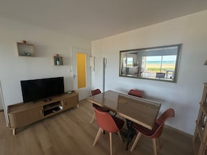 A modern living room with a flat-screen TV, wooden entertainment unit, and a dining table with red chairs. - Apartment, sea view, pets welcome - 4 guests (Cabourg)