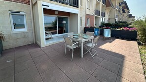Un immeuble résidentiel doté d’un patio comprenant une table et des chaises, une grande fenêtre et un balcon avec des balustrades.