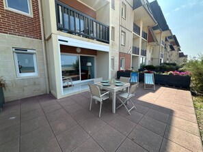 A residential building with a patio area featuring a table and chairs, a large window, and a balcony with railings. - Apartment, sea view, pets welcome - 4 guests (Cabourg)