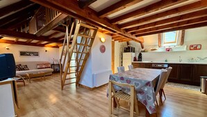 Een eetgedeelte met een tafel voor vier personen, houten stoelen en een ladder naar een hoger niveau.