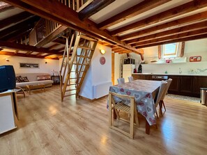 Ein Essbereich mit Tisch für vier Personen, Holzstühlen und einer Treppe zu einer oberen Ebene.