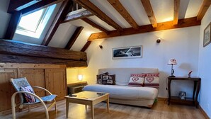 Een knus interieur met een houten plafond, een bank met gestreepte kussens, een bijzettafeltje en een stoel.
