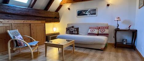 A cozy room with a wooden ceiling, a sofa with patterned cushions, a small table, and a chair.