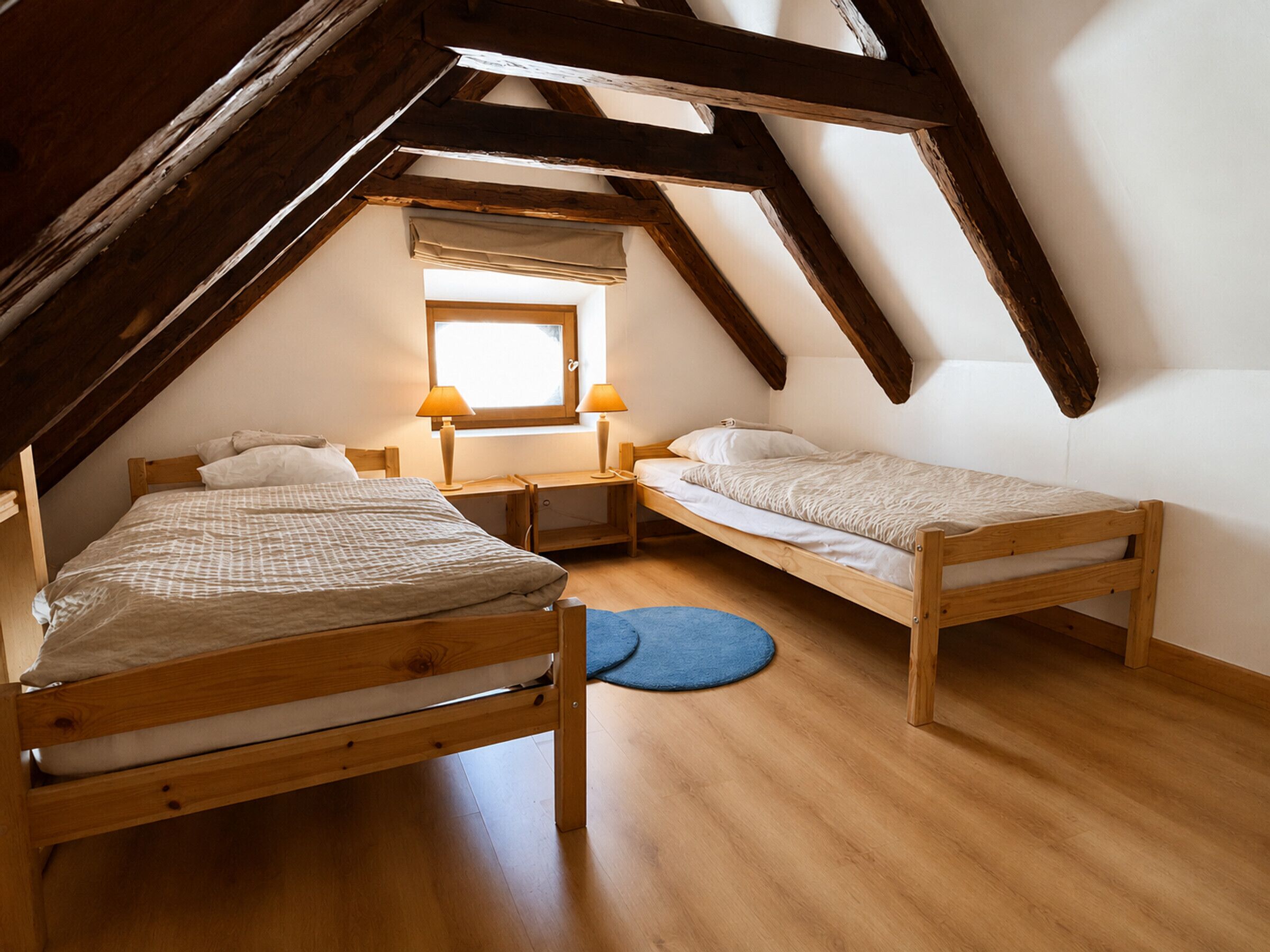 Une chambre de dortoir avec deux lits superposés en bois, une fenêtre avec un store et un tapis bleu sur le sol.