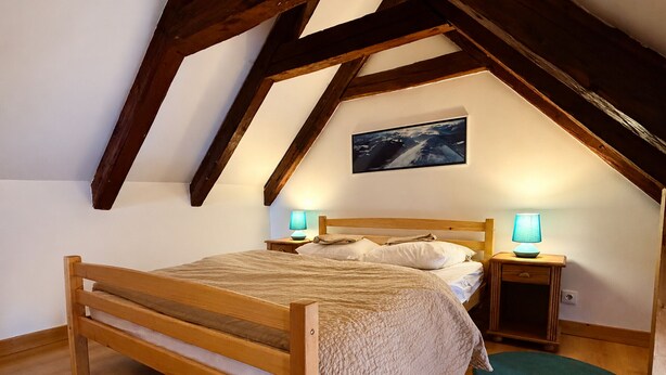 Een slaapkamer met een houten bed, twee nachtkastjes met lampen, een aan de muur hangend schilderij en een houten plafond.