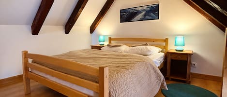 Un dormitorio con una cama de madera, dos mesitas de noche con lámparas, un cuadro en la pared y techo de madera.