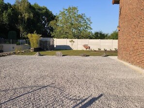 Une allée de gravier mène à un bâtiment en briques, et une zone délimitée par une clôture abrite une sculpture de cerf.