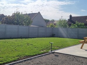 A backyard with a concrete wall, a grassy area, and a wooden bench.