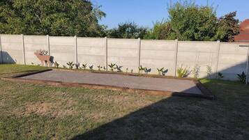 Une zone pavée, avec un mur en béton et une rangée de plantes.