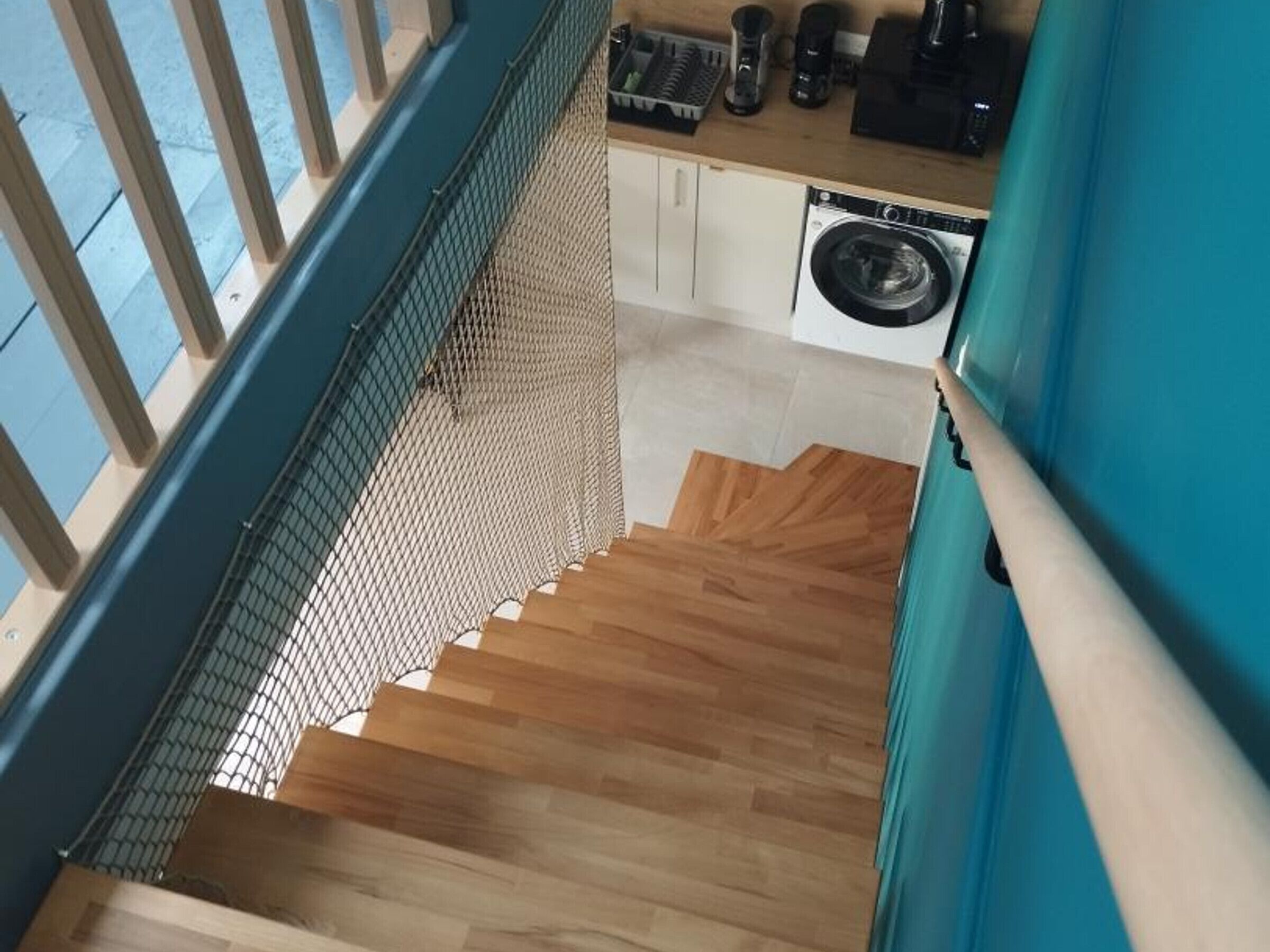 Un escalier avec des marches recouvertes de bois, menant à une cuisine équipée d’un lave-linge et de divers appareils électroménagers.