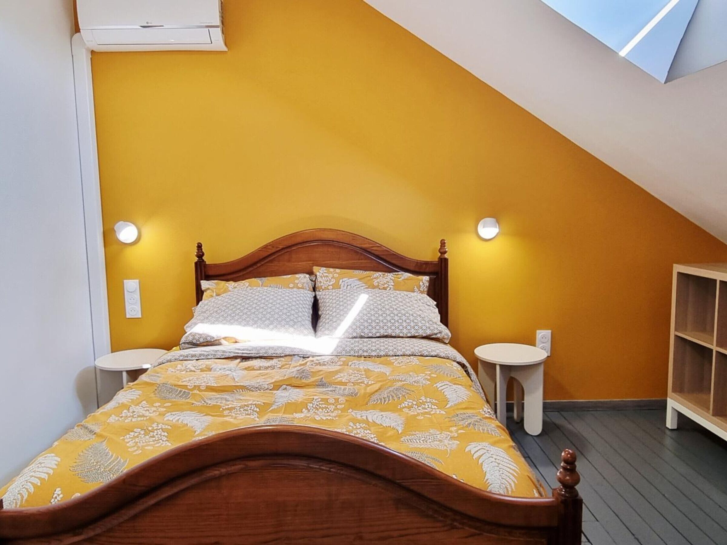 Een slaapkamer met een schuine plafond, een houten bed, twee nachtkastjes en een inbouwkast.