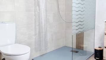 Une salle de bain comprenant des toilettes, un espace douche et un mur carrelé.