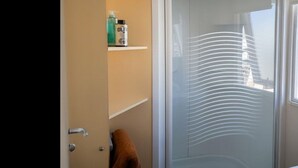 A bathroom with a glass shower door, a towel hanging on the door, and toiletries on a shelf. - Air-conditioned mobile home - 6 guests (Caves)
