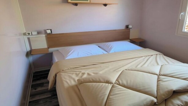 A hotel room with a bed, a nightstand, a wall-mounted clock, and a window. - Air-conditioned mobile home - 6 guests (Caves)