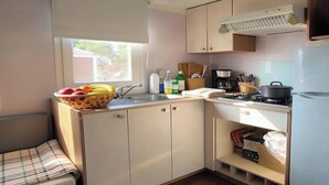 A compact kitchenette with a sink, stove, and a small refrigerator. - Air-conditioned mobile home - 6 guests (Caves)