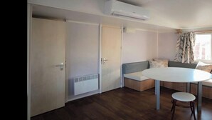 A room with a round table and two chairs, a sofa, and a window with curtains. - Air-conditioned mobile home - 6 guests (Caves)